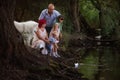 Diversity family of four launching white origami boat into water. Samoyed dog. Traveling with pets Royalty Free Stock Photo