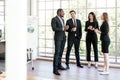 Diversity group of businesspeople strictly dressed in the suits standing meeting by office window. African and Caucasian. Royalty Free Stock Photo