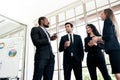 Diversity group of businesspeople strictly dressed in the suits standing meeting by office window. African and Caucasian white. Royalty Free Stock Photo
