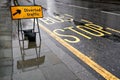 Diverted traffic black and yellow sign on wet pavement, next to road with Bus Stop text, lights reflect in rain covered asphalt Royalty Free Stock Photo