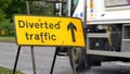 Diverted traffic sign with cars and trucks passing on background on british road