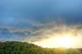 Divine rays from under dark storm clouds after a hurricane over a green forest hill with trees Royalty Free Stock Photo