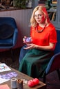 Diviner wearing skirt and red blouse sitting in armchair and reading cards