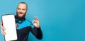 Diving guy showing okay gesture and smartphone with empty white screen display for new Application on blue studio wall background Royalty Free Stock Photo