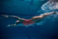 Diving into water. Professional female swimmer in cap and goggles training in swimming pool indoor. Underwater view Royalty Free Stock Photo