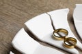 Divorce concept. Broken plate and rings on wooden table, closeup Royalty Free Stock Photo