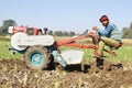 Indian farmer man driving small tractor for soil cultivation and wheat planting.