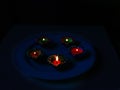 5 Lit diyas placed on a plate with dark background