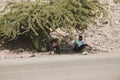 A Djiboutian man and his two sons sitting on the stone and waiting the bus under a tree`s shade in Djibouti. Editorial shot in Royalty Free Stock Photo