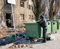 Homeless man searches for food and books in a dumpster. Selective focus, street photo, Royalty Free Stock Photo