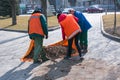 Two men and a woman collect old dry leaves in a spring park in a plastic bag. Municipal