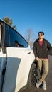 A man leans against a white vehicle on a paved road under a clear blue sky. Royalty Free Stock Photo