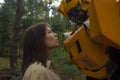 Portrait of a robot transformer Bumblebee and girl standing together among forest