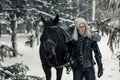 Cosplayer in image of a character Geralt of Rivia from the game or film The Witcher next to a horse in winter forest