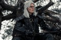 Portrait of cosplayer in image of character Geralt of Rivia from the game or film The Witcher with sword in winter forest