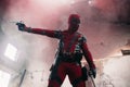 DNIPRO, UKRAINE - MARCH 28, 2019: Deadpool cosplayer posing indoors with guns on background of smoke