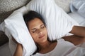 Do I have to get up for work. A beautiful young woman holding a pillow to her ears as she lays in bed. Royalty Free Stock Photo