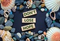 Do not lose hope symbol. Words `Do not lose hope` on wooden blocks on a beautiful black background. Sea stones and seashells.