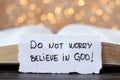 Do not worry, believe in God, handwritten Christian text on paper note in front of open holy bible with bokeh light background
