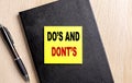 DO\'S AND DONT\'S text on a sticky on black notebook with pen