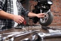 Do it yourself, hands repairing a motorcycle in the garage with red brick wall, pegboard work tools and wrenches in the work bench