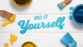 Do it yourself text on a white wooden table surrounded by color brushes, boxes and few color drops