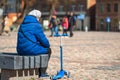 an old woman rests on a bench waiting for her grandchild to play in the town square, rear view