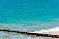 Dock pilings on a sandy beach, blue ocean and yellow sand, sunny