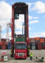 Dock straddle carrier loading a shipping container onto a trailer being pulled by a red Renault Magnum truck