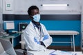 Doctor of african american ethnicity sitting at desk with face mask Royalty Free Stock Photo