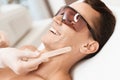 The doctor applies an epilation gel on the man`s face. The man laughs, because he is ticklish.