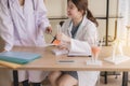 Doctor 2 asian woman sitting and working on desk using foot fingers plastic anatomy physiology model a bones and hand pointing or Royalty Free Stock Photo