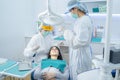 Doctor and assistance in protective masks serving Asian young woman patient by examining teeth or dental checkup at dental clinic.