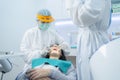 Doctor and assistant in PPE wear protective facemask due to Covid19, examining young woman patient`s teeth or dental checkup at de Royalty Free Stock Photo