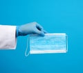 Doctor in blue latex sterile gloves holds a blue disposable mask made of non-woven material on a blue background Royalty Free Stock Photo