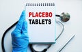 A doctor in blue medical gloves holds a notebook with the inscription PLACEBO TABLETS, on the background of a light table, along