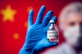 A doctor in blue medical gloves and mask holding an ampula with vaccine in front of flag of China. Close up shot. Coronavirus,