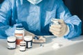 Doctor in a blue surgical gown and mask holds in his hand a medicine bottle. Many pills and drugs on white table, healthcare