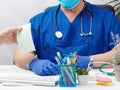 Doctor in blue uniform and latex gloves sits at a white table and leads a patient reception