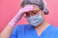 The doctor in a blue uniform on a pink background tiredly bowed her head, copy space. Sad nurse face with glasses, beret and Royalty Free Stock Photo