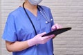 A doctor in a blue uniform presses a finger on the tablet screen. Nursing with a stethoscope with an electronic tablet in hand