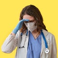 The doctor in a blue uniform on a yellow background tiredly bowed her head, copy space. Sad nurse face with medical mask