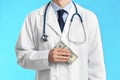 Doctor with bribe on light blue background. Corruption in medicine Royalty Free Stock Photo