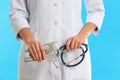 Doctor with bribe and stethoscope on light blue background, closeup. Corruption in medicine Royalty Free Stock Photo