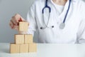 Doctor building pyramid of blank wooden cubes on table against grey background, closeup. Space for text Royalty Free Stock Photo