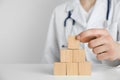 Doctor building pyramid of blank wooden cubes on white table against light background. Space for text Royalty Free Stock Photo