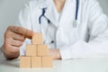 Doctor building pyramid of blank wooden cubes on white table against light background, closeup. Space for text Royalty Free Stock Photo