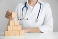 Doctor building pyramid of blank wooden cubes on white table against light background, closeup. Space for text Royalty Free Stock Photo