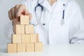 Doctor building pyramid of blank wooden cubes on white table against light background. Space for text Royalty Free Stock Photo