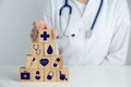 Doctor building pyramid of wooden cubes with different icons at white table, closeup. Insurance concept Royalty Free Stock Photo